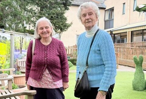 two older ladies standing outside in a garden